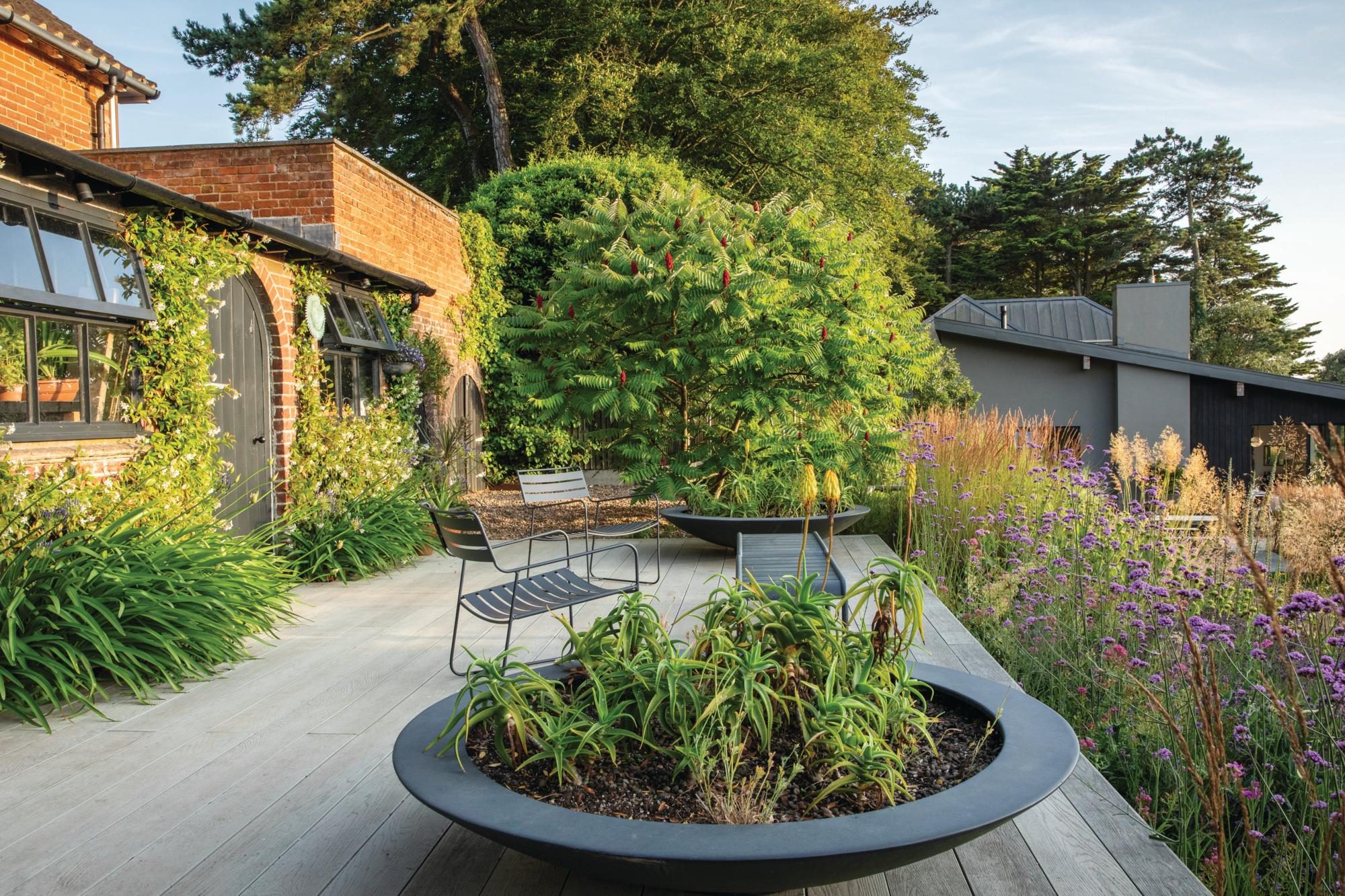 A patio with green plants edging and a brick house