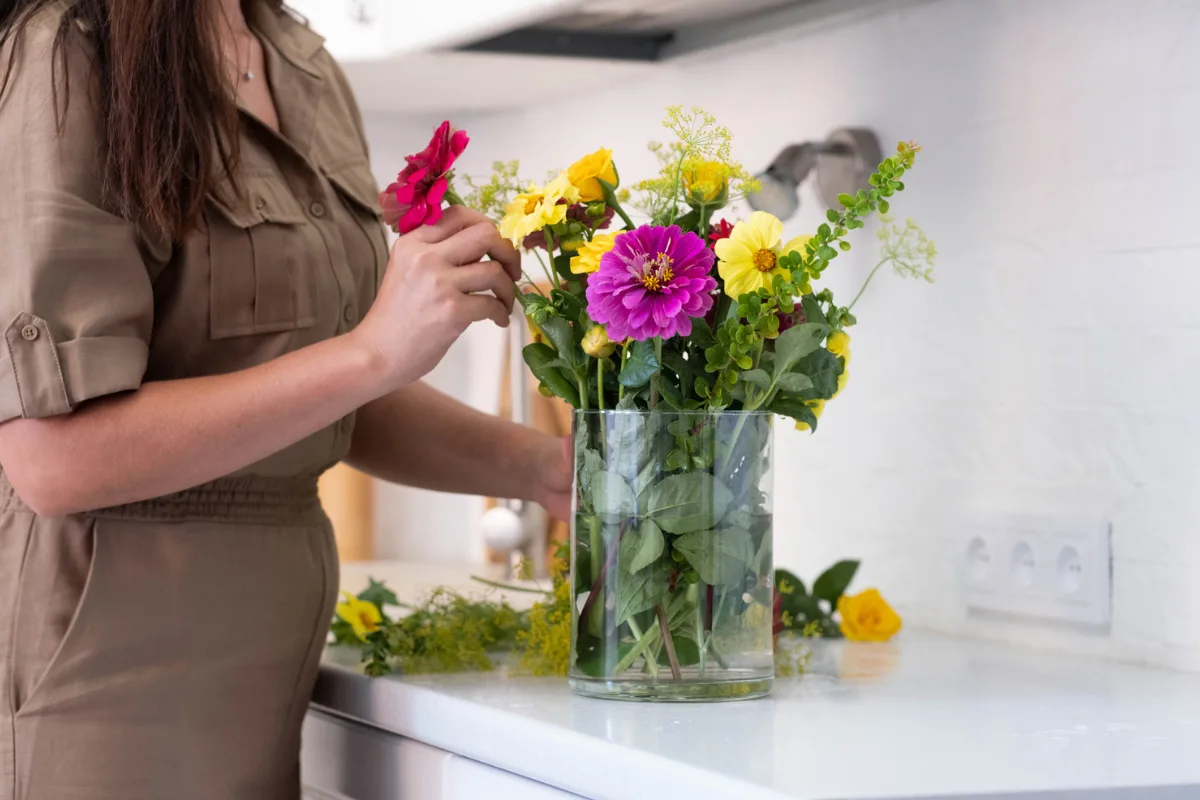 arranging-bouquet A woman arranging a colourful bouquet in a decorative vase on a kitchen counter.